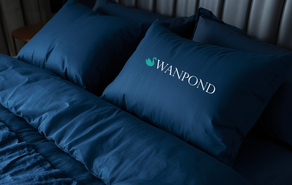 Swanpond eco resort logo design — teal swan mark and white wordmark on a navy pillow in a moody luxury resort bedroom
