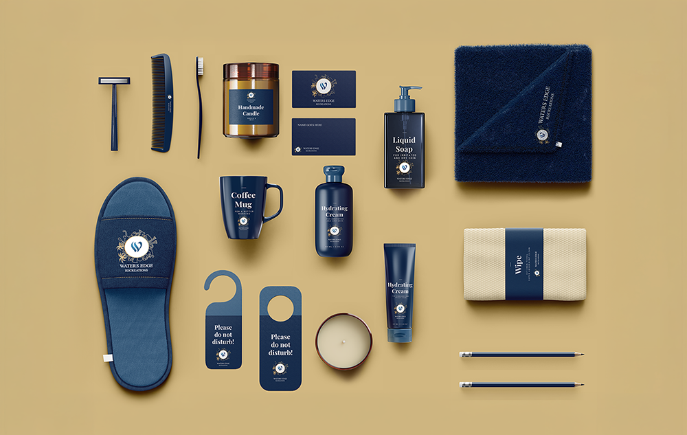 Waters Edge Recreations recreation logo design — navy blue branded merchandise flatlay showing slippers coffee mug candle liquid soap hydrating cream door hangers business cards towel wipe and pencils on a gold background