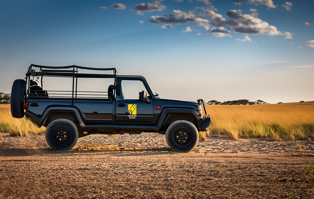 Leopard Safari safari logo design on a black open top safari jeep door with yellow claw paw icon and wordmark parked on a sandy African plain under a blue sky with golden grass